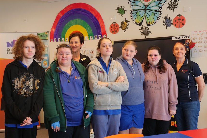 A group of teenage students in a brightly decorated classroom.