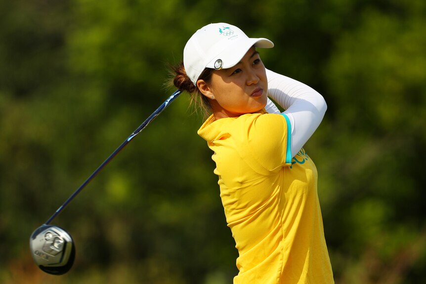 Minjee Lee wearing a yellow shirt and white cap swinging a golf club