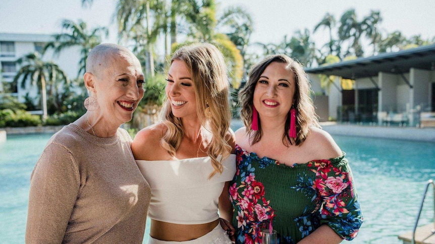 Image of three women, left older woman with cancer and shaved head, middle young woman, right young women all staring at mother.