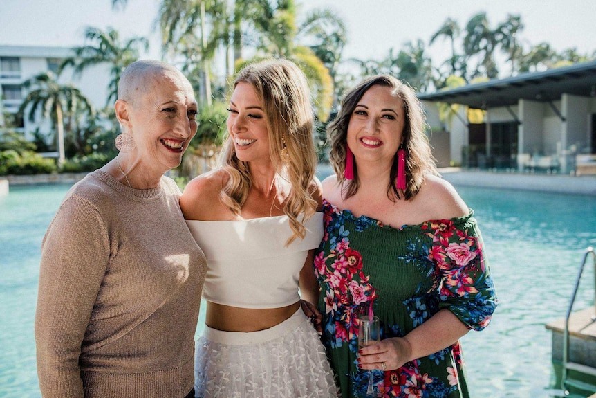 Image of three women, left older woman with cancer and shaved head, middle young woman, right young women all staring at mother.