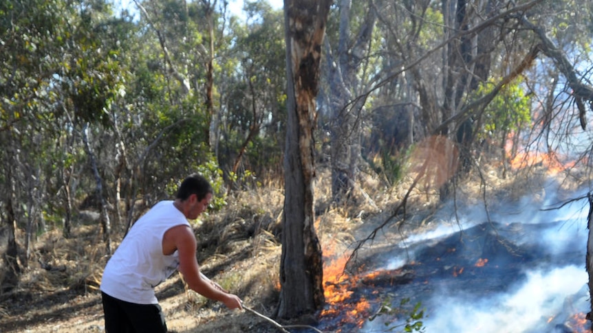 Roleystone locals Derryn Grosse (foreground) and Bennett Moran battle a bushfire using a rake and a gum tree branch
