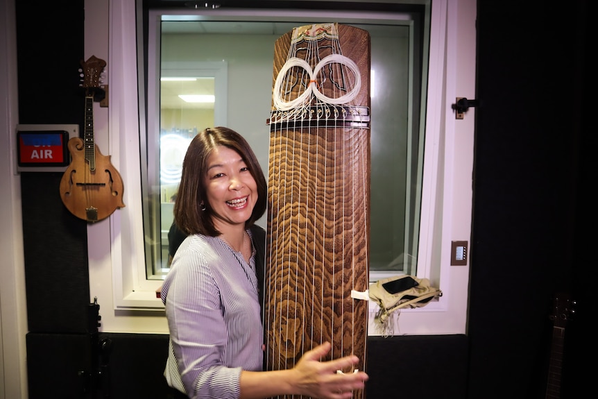 Woman smiling, holding a Koto upright.