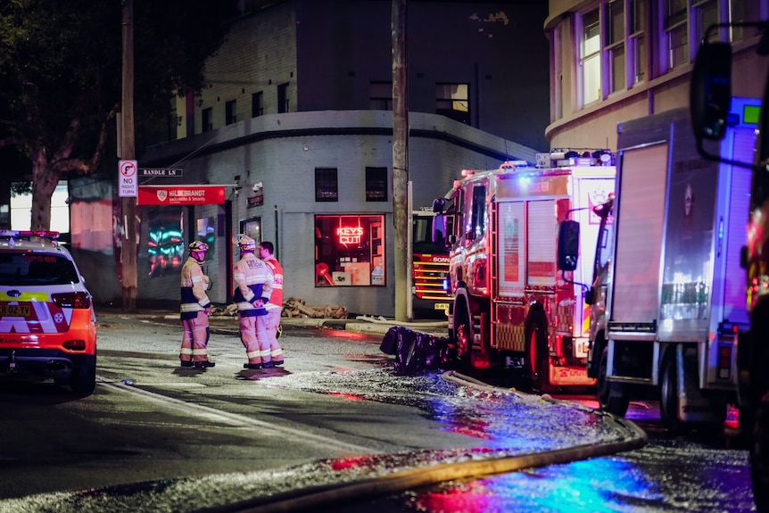 firefighters standing outdoors as water gushes down a street