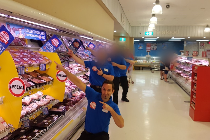 Daragh and three other Coles staff in uniform pose for a photo pointing at a meat display.