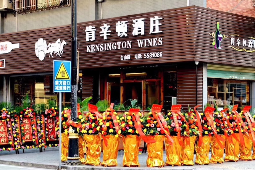 a corner-street store in the background with kensington wines in english and chinese, with bright floral displays in front.