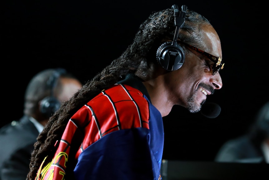 Snoop Dogg smiles wearing a comment headset