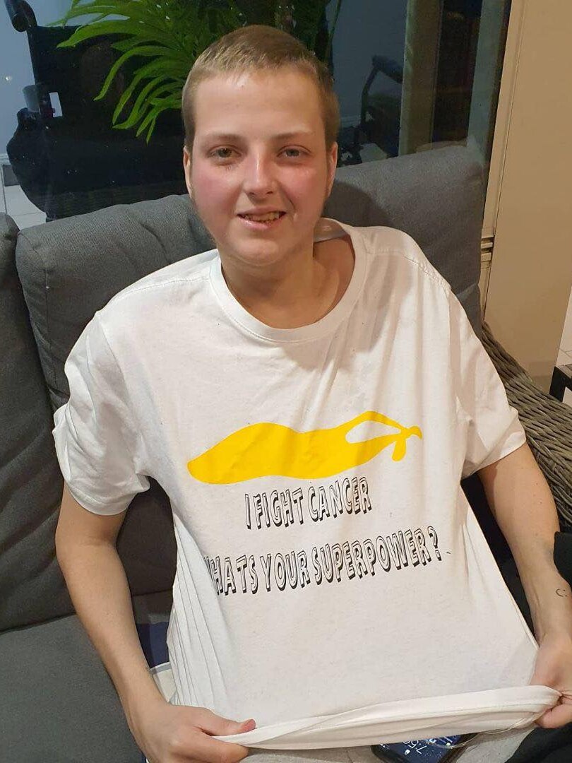 A young man wearing a t-shirt that reads "I fight cancer, what's your super power".