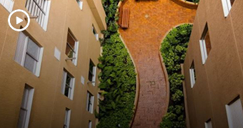 A bird's eye view image of curved brick path between two tall buildings, with shrubbery to the sides.