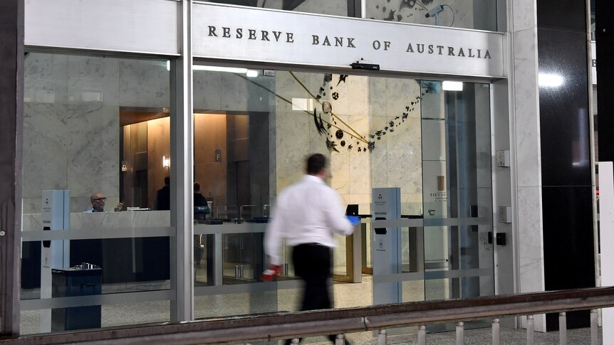 A person in a long sleeved white collared shirt and black pants walks into the Reserve Bank of Australia as its doors slide open