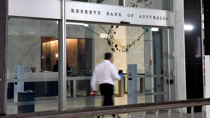 A person in a long sleeved white collared shirt and black pants walks into the Reserve Bank of Australia as its doors slide open