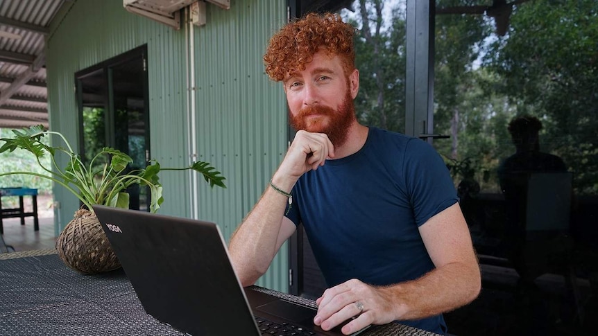 A red haired filmmaker Phil Denson at a table with his laptop