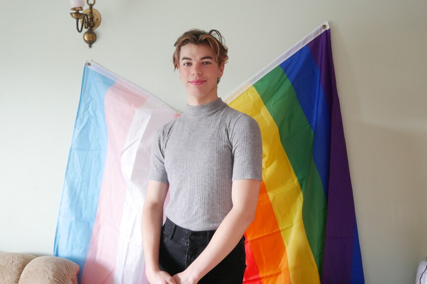 Woman standing in front of queer and transgender flags in grey t-shirt smiling