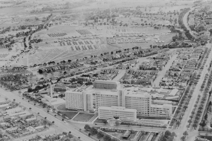 A black and white postcard showing Camp Argus in Royal Park from the air with the Royal Melbourne Hospital in the foreground.