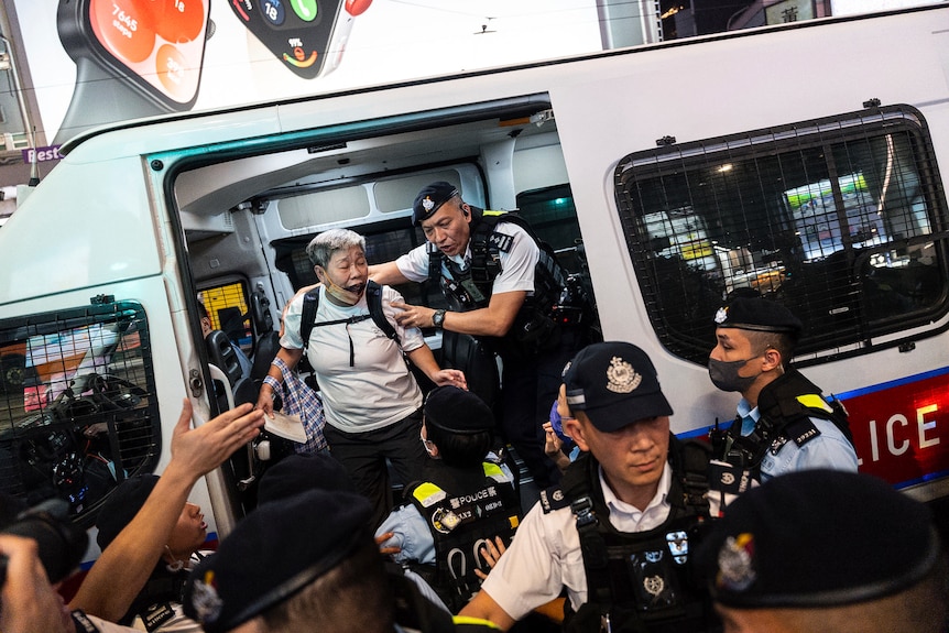 A woman is held in a police van by a policeman with other officers around