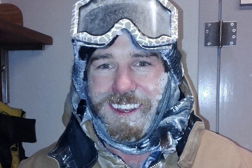 A man with skiing googles on his forehead and a frozen beard smiles for a story on working as a plumber in Antarctica
