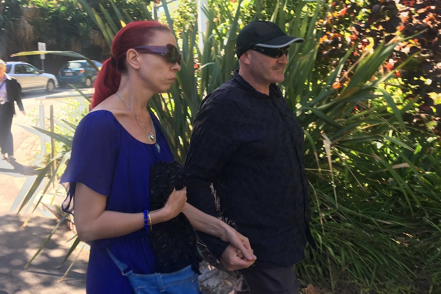 A woman in a blue dress and man in a black t-shirt hold hands as they walk outside court.