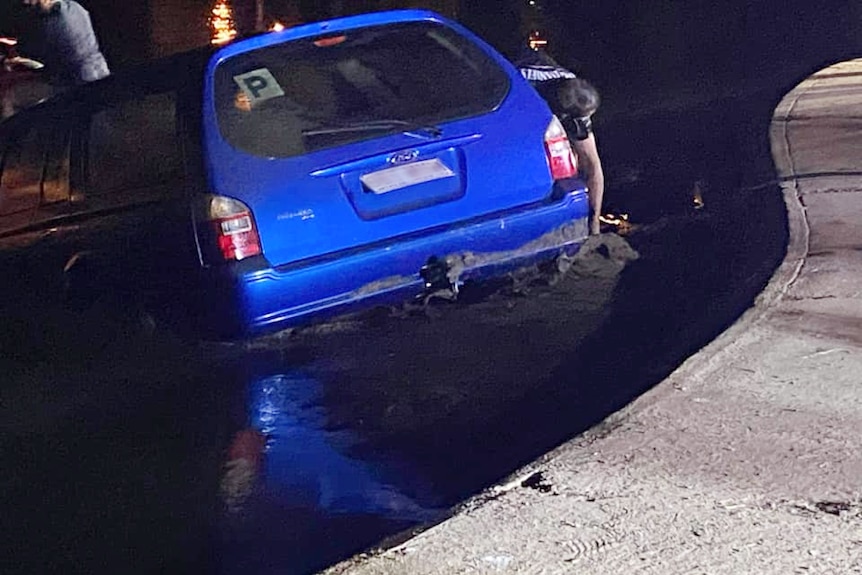 A blue car with P plates submerged in water.