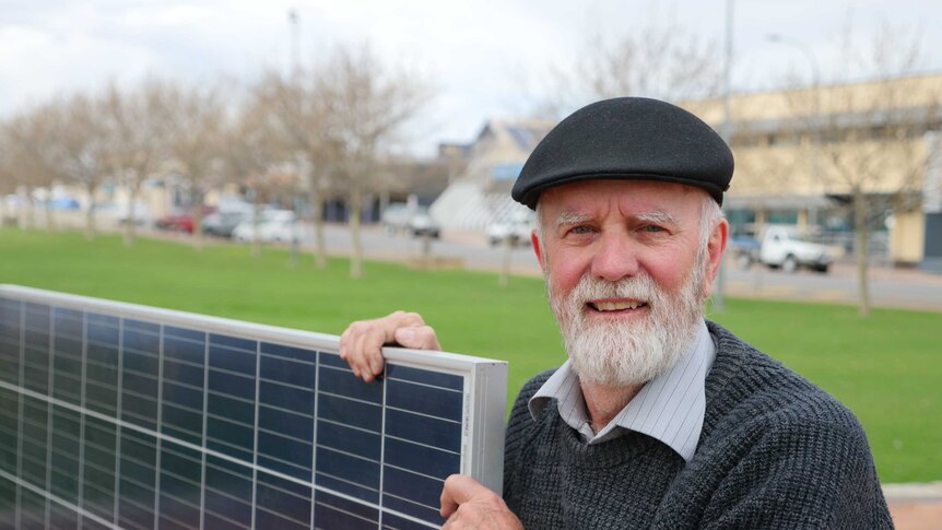 A man standing outside holding a large solar panel.