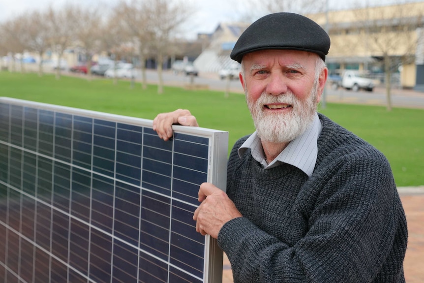 A man standing outside holding a large solar panel.