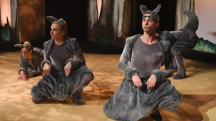 Four actors on stage dressed as grey kangaroos crouch and look towards the audience.