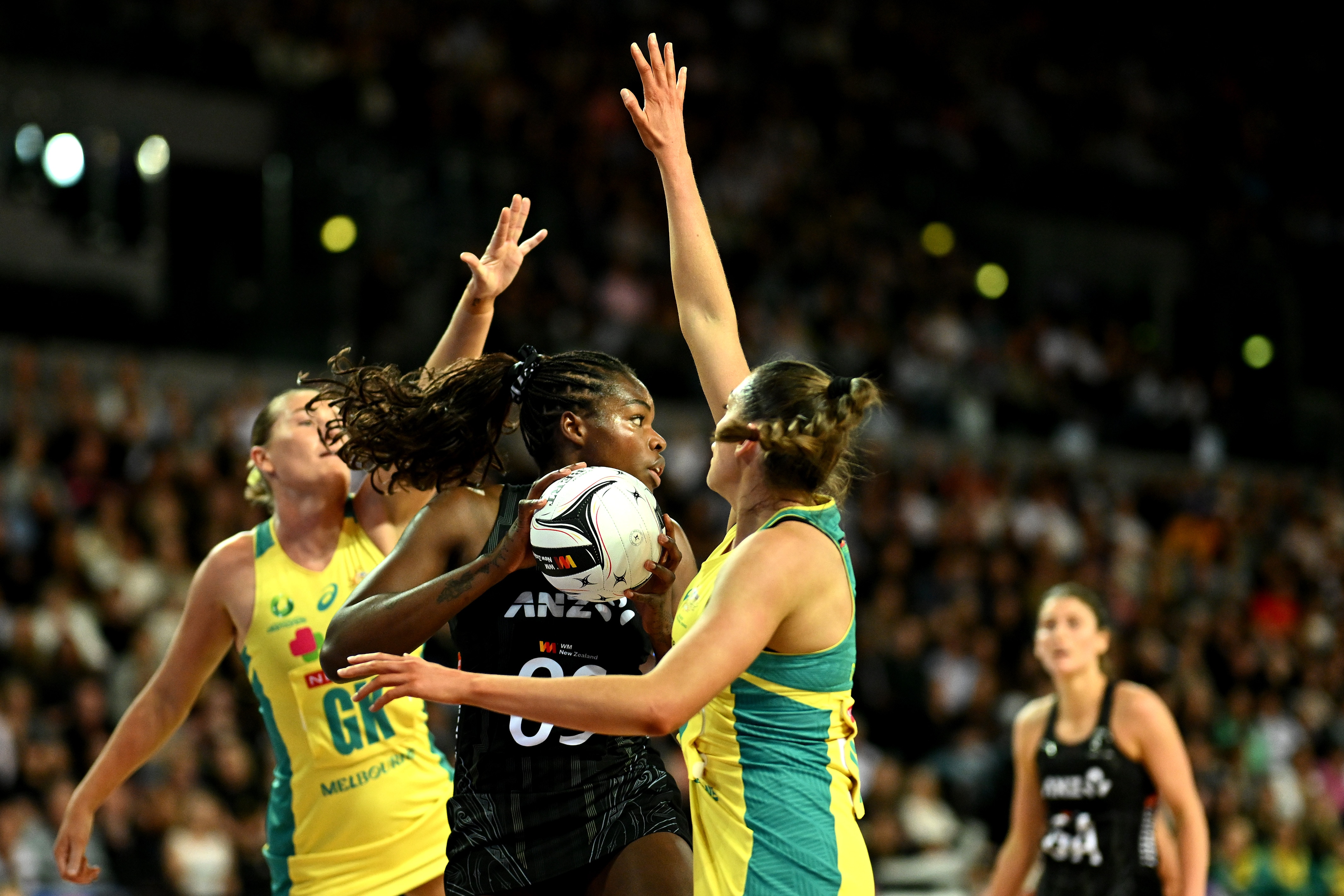 A player takes the ball despite being challenged by two opposing players either side of her