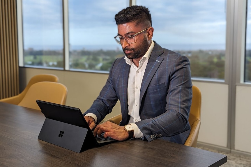 Man in suit working on laptop in office board room.  