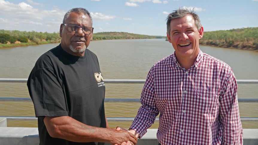 two men shaking hands on a bridge over a river.