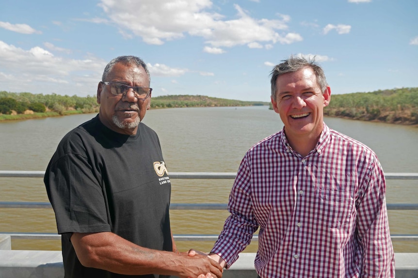 two men shaking hands on a bridge over a river.