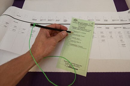 A person holds a pen over a ballot form in a polling booth.