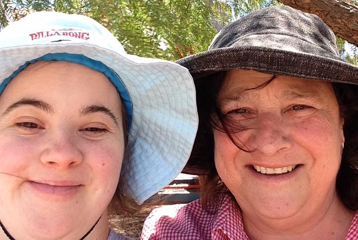 Two women with sun hats on smiling, trees behind.