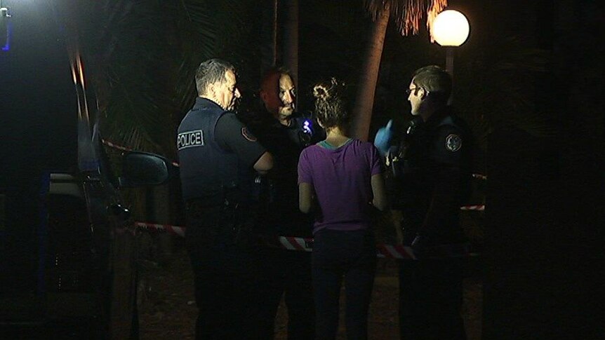 Three police officers talk to a young woman in a purple t-shirt with a red tape police line between them.