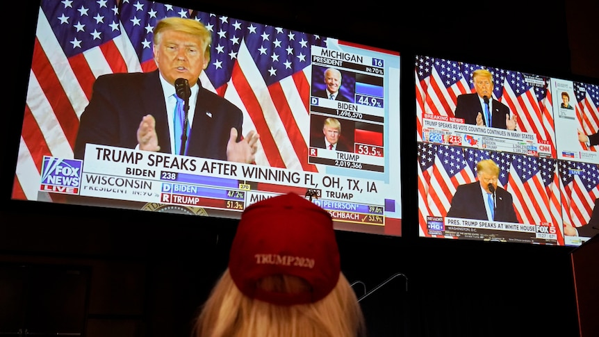 An image of a woman from behind watching US President Donald Trump on multiple TV screens.