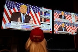 An image of a woman from behind watching US President Donald Trump on multiple TV screens.
