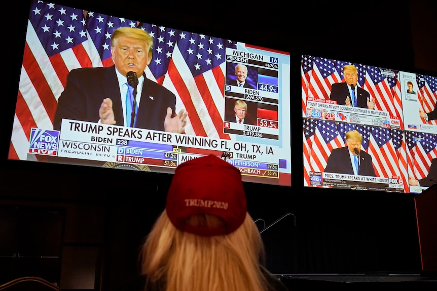 An image of a woman from behind watching US President Donald Trump on multiple TV screens.