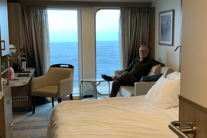 John Kable sits in a cruise ship cabin. The ocean can be seen out the window.