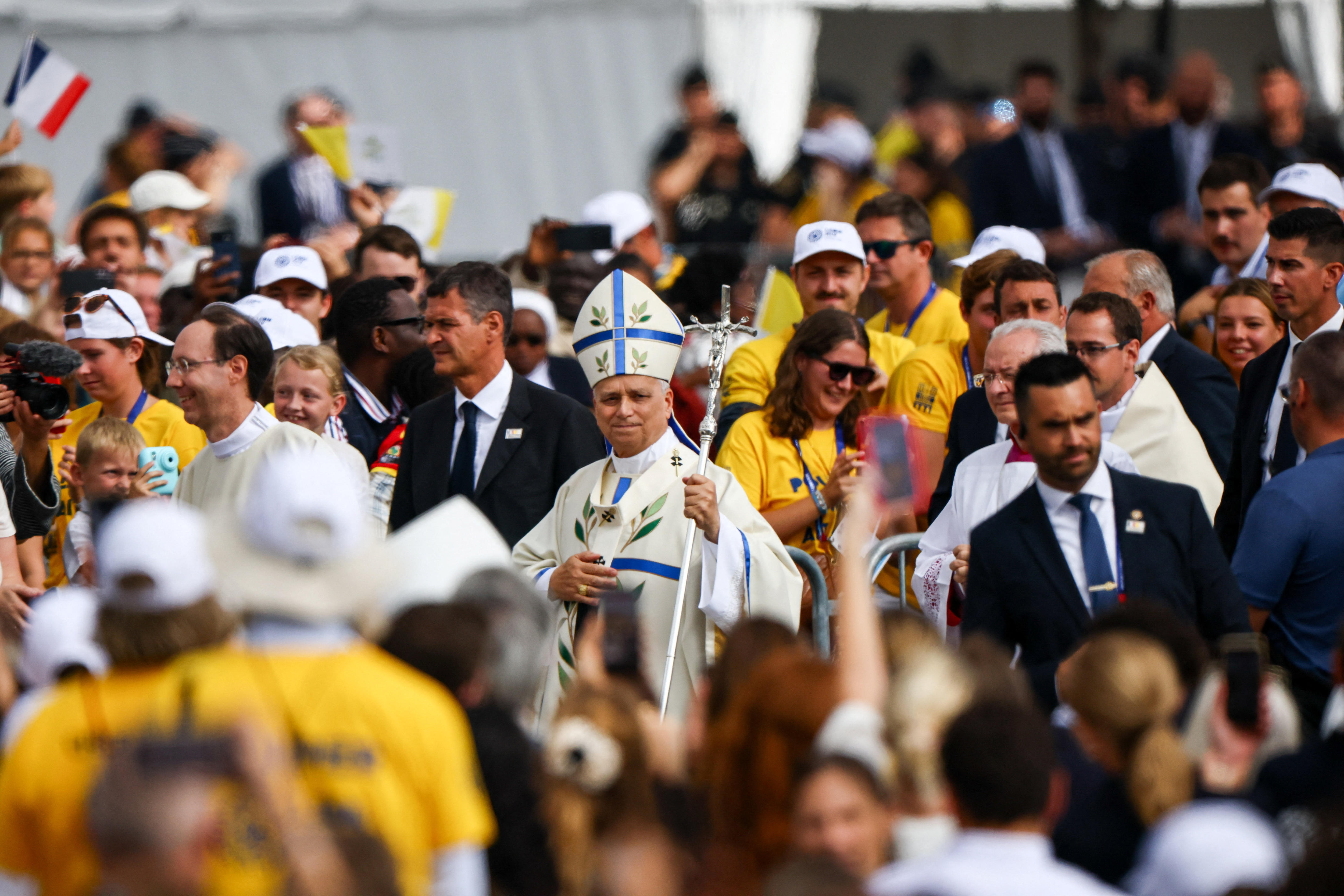 Pope Leo walks through a crowd wearing a clerical gown, a tall hat and holding the Papal ferula.