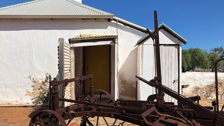 A piece of farm machinery outside the Oakabella Homestead and an outdoor toilet to the side.