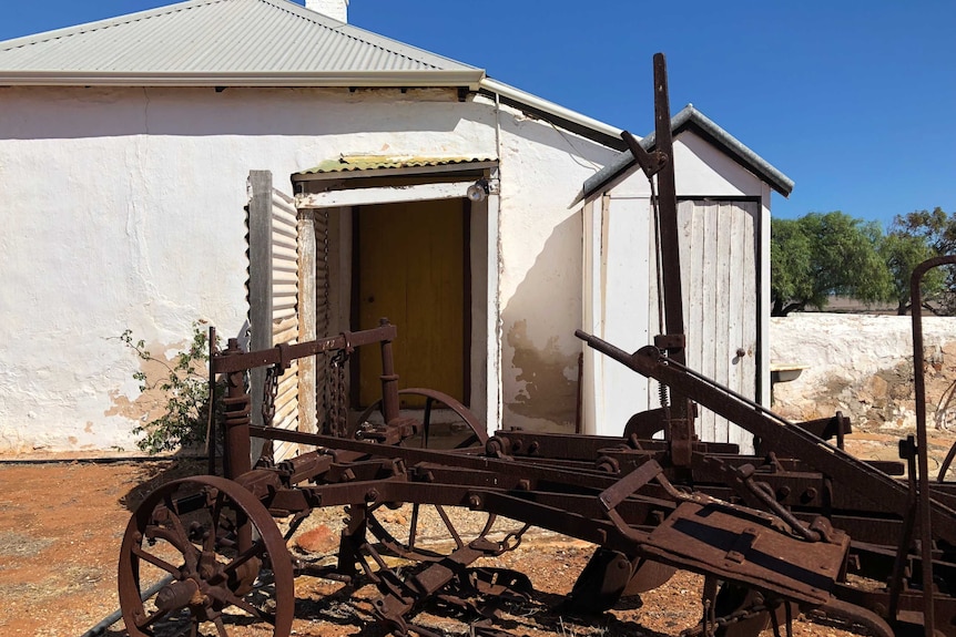 A piece of farm machinery outside the Oakabella Homestead and an outdoor toilet to the side.