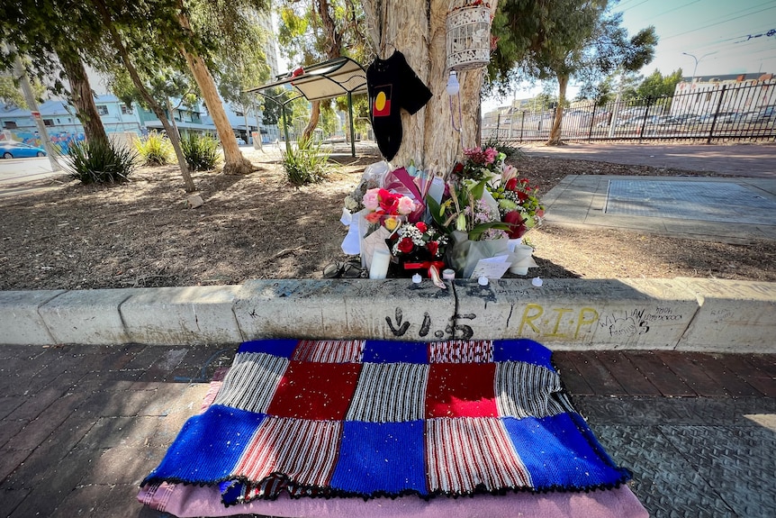 A knitted rug and bouquets of flowers underneath an inner city tree