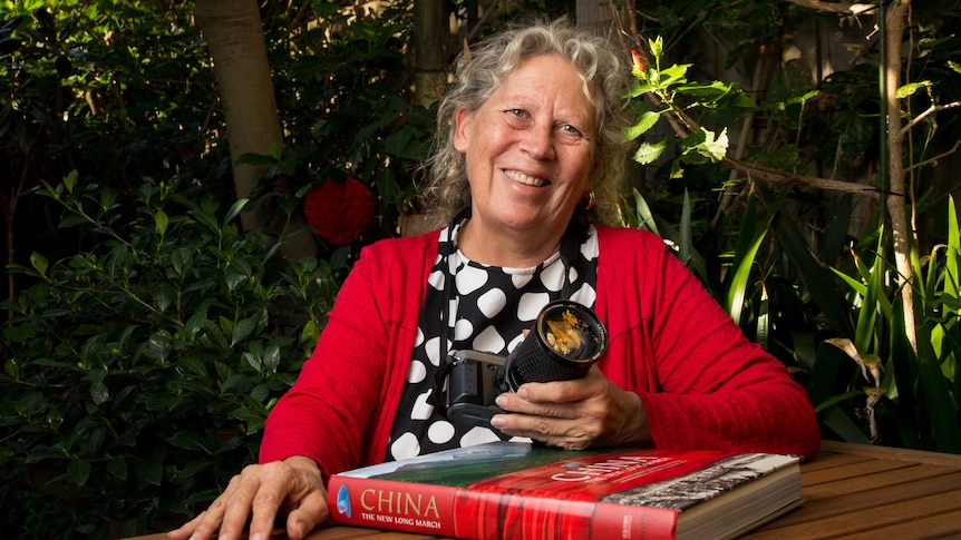 Catherine Croll sits at a table holding her camera.