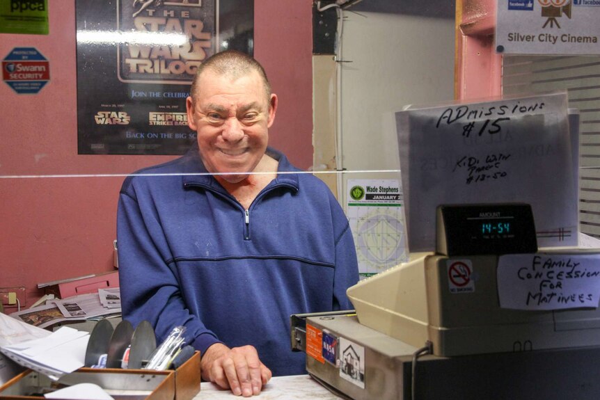 A man in a blue windcheater stands at the ticket counter of a cinema.