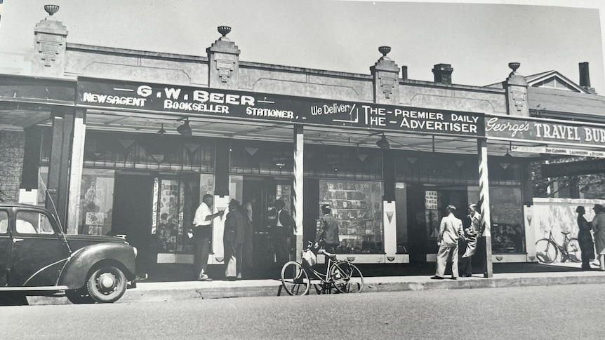 Old fashioned black and white photo of shopfront with men meeting in pairs out the front from 1940s
