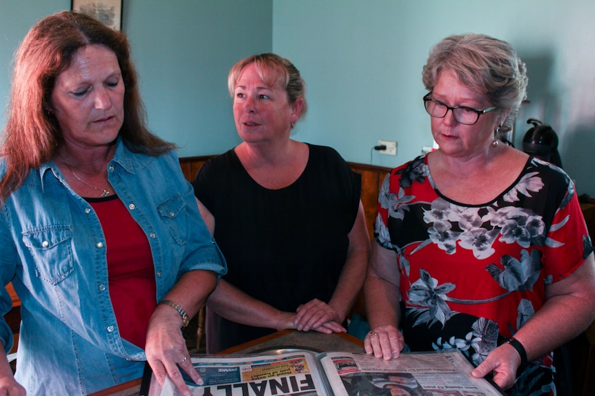Lyn Ireland, Jodie MacDonell and Debra MacDonell look at a newspaper.