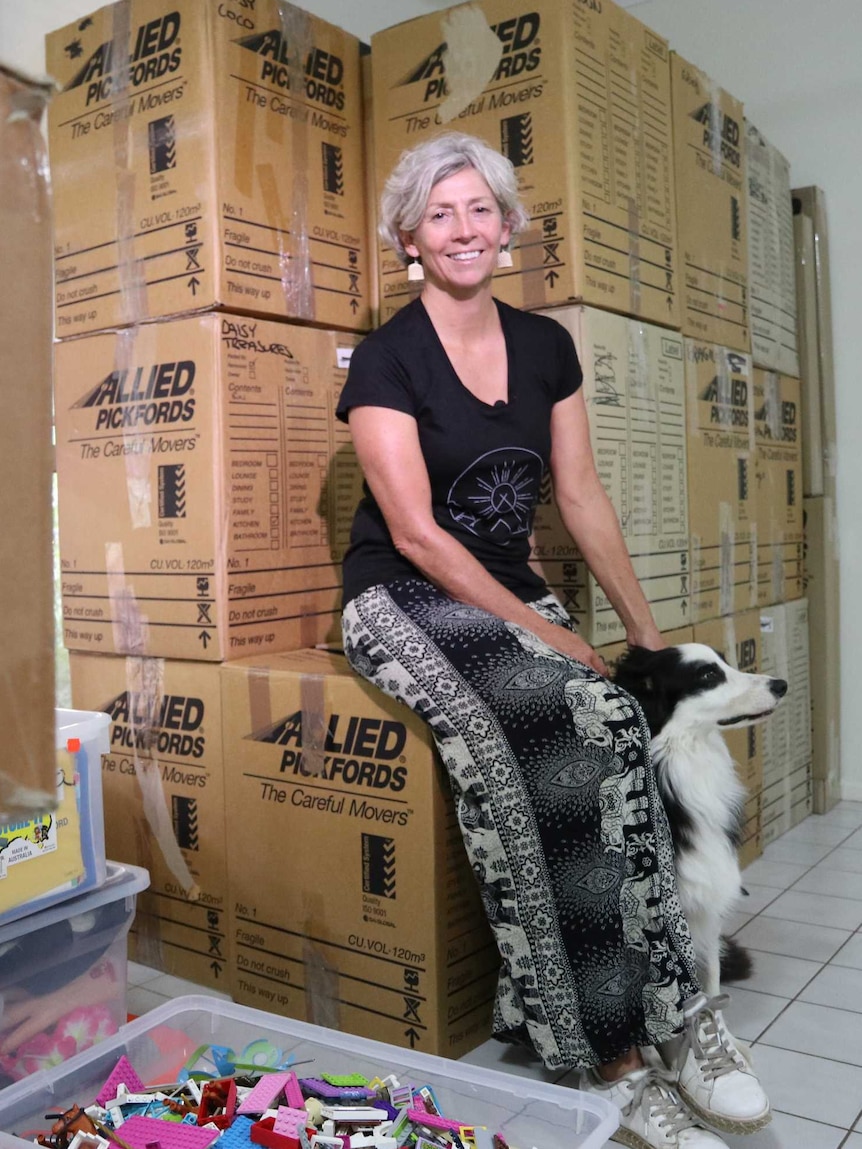 Denise House, a Jabiru resident, sitting on a pile of packing boxes, next to her dog.