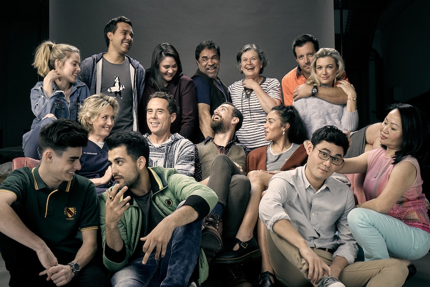 The cast of The Heights sit in a photography studio, all stationed around or sitting on a couch, looking happily at one another.