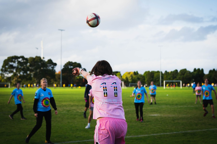 The back of a person wearing a pink shirt, throwing the football onto the field.