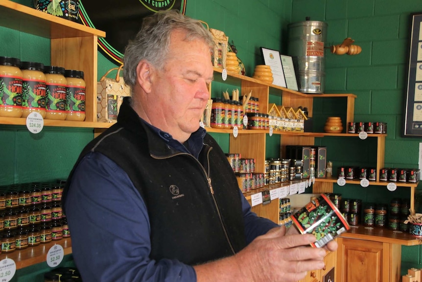 A man stands inside a shop looking at a tin of honey with shelves of product behind him.