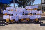 Primary school kids holding up decorated pillowcases in front of a playground.  