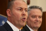 Josh Frydenberg's lips are pursed as he speaks. In the background, somewhat out of focus, Mathias Corman smirks.