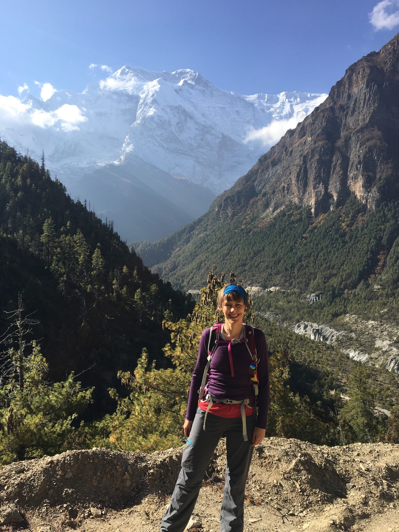 A woman wearing hiking clothes and smiling and standing in front of mountains.